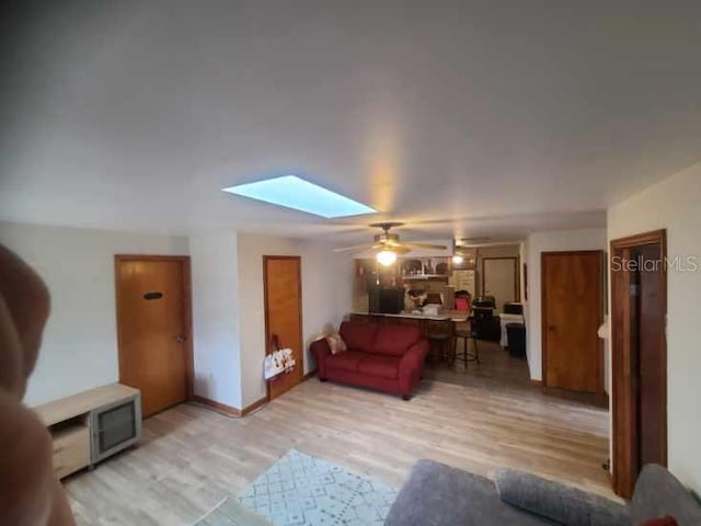 living room with light hardwood / wood-style flooring, a skylight, and ceiling fan