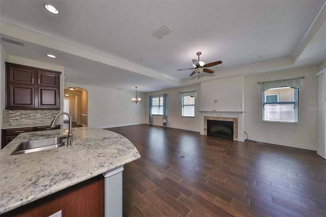 kitchen featuring dark wood-type flooring, ceiling fan with notable chandelier, sink, a fireplace, and tasteful backsplash