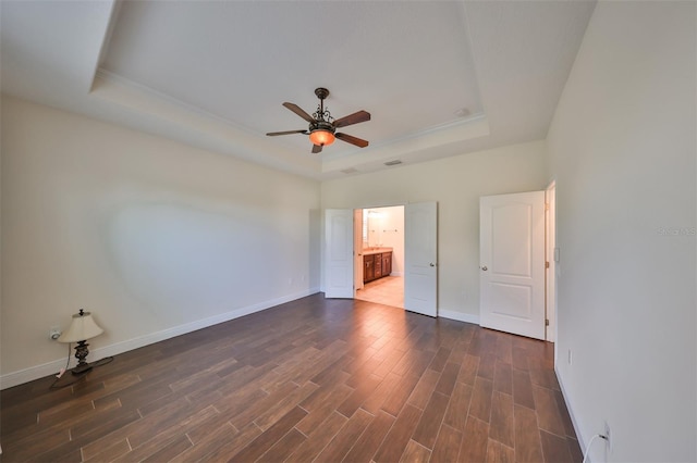 unfurnished bedroom with dark hardwood / wood-style floors, a raised ceiling, ceiling fan, and ensuite bathroom