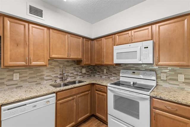 kitchen featuring white appliances, backsplash, sink, light stone countertops, and a textured ceiling