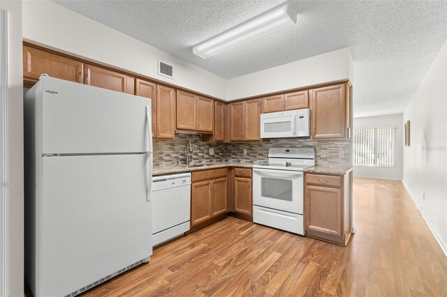 kitchen with white appliances, backsplash, sink, light hardwood / wood-style flooring, and light stone counters