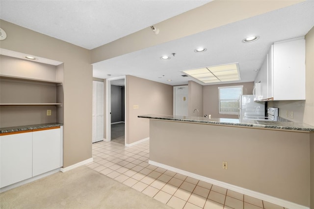 kitchen with light stone countertops, light carpet, refrigerator, kitchen peninsula, and white cabinetry