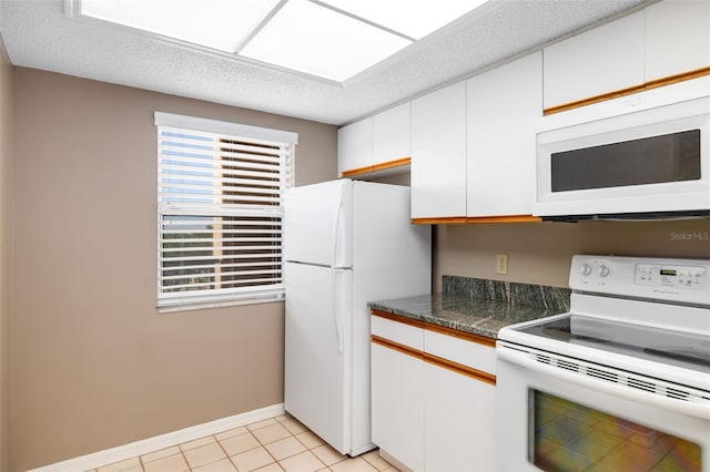 kitchen with white cabinets, dark stone countertops, a textured ceiling, white appliances, and light tile patterned floors