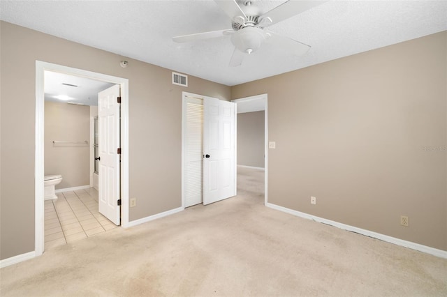 unfurnished bedroom featuring ceiling fan, ensuite bathroom, light colored carpet, a textured ceiling, and a closet