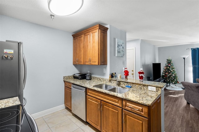 kitchen featuring brown cabinetry, light stone counters, open floor plan, stainless steel appliances, and a sink