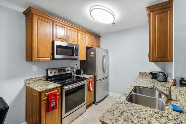 kitchen with light stone countertops, brown cabinetry, stainless steel appliances, and a sink