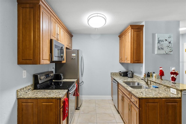 kitchen featuring stainless steel appliances, brown cabinetry, a sink, and light stone countertops