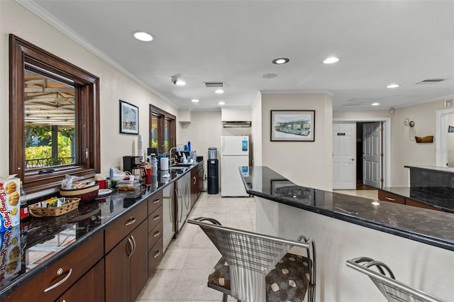 kitchen featuring dark stone counters, white refrigerator, sink, ornamental molding, and dark brown cabinets