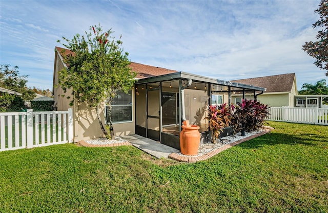 back of house featuring a yard, a sunroom, fence, and stucco siding