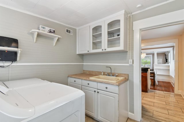 laundry room with washing machine and clothes dryer, sink, cabinets, wood walls, and light wood-type flooring