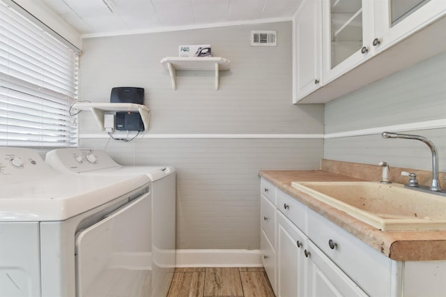 laundry room with cabinets, sink, light hardwood / wood-style flooring, washing machine and dryer, and wood walls