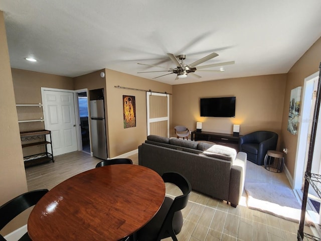 living room with ceiling fan, a barn door, and light wood-type flooring