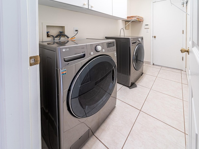 laundry area with washer and dryer, light tile patterned flooring, and cabinets