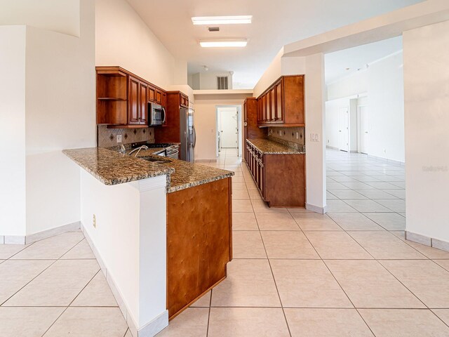 kitchen with backsplash, light tile patterned flooring, kitchen peninsula, and stainless steel appliances