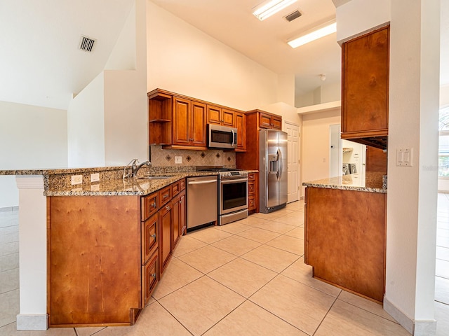 kitchen with sink, light tile patterned flooring, light stone counters, kitchen peninsula, and stainless steel appliances