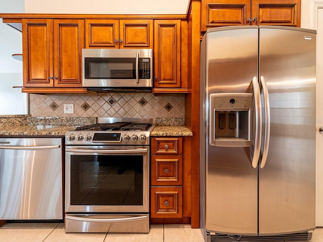 kitchen featuring backsplash, light stone counters, light tile patterned floors, and appliances with stainless steel finishes