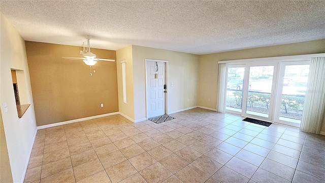 empty room with ceiling fan, light tile patterned flooring, and a textured ceiling