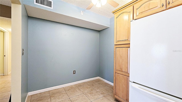 interior space featuring a textured ceiling, ceiling fan, light brown cabinets, white fridge, and light tile patterned flooring