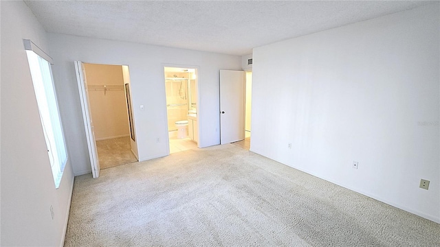 unfurnished bedroom featuring a spacious closet, a textured ceiling, connected bathroom, light colored carpet, and a closet