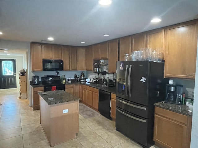 kitchen with dark stone counters, sink, black appliances, light tile patterned floors, and a kitchen island