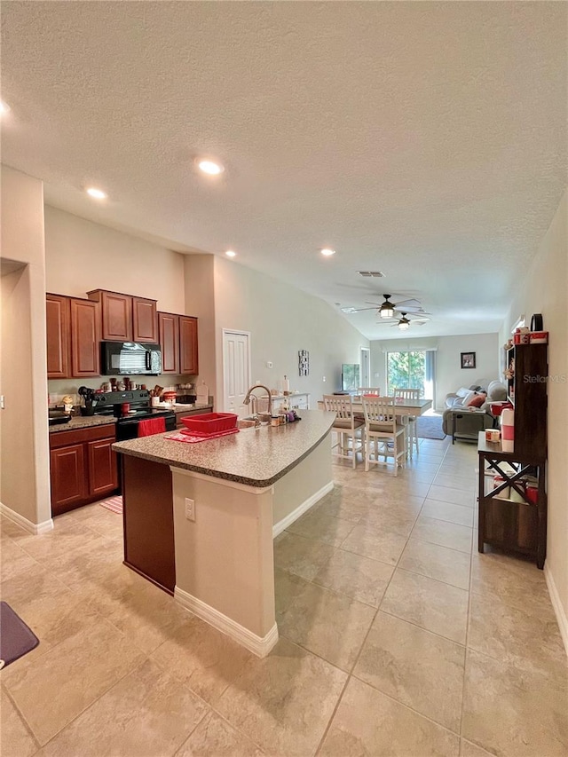 kitchen featuring ceiling fan, sink, an island with sink, a textured ceiling, and black appliances