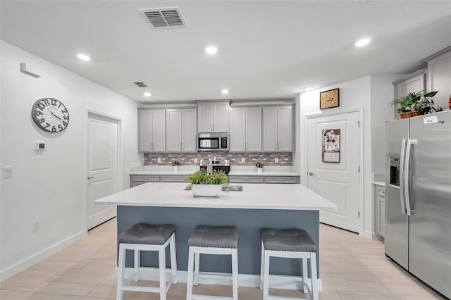 kitchen with a breakfast bar, decorative backsplash, a center island with sink, and appliances with stainless steel finishes