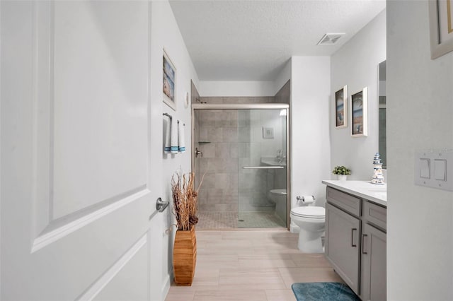 bathroom featuring a shower with door, vanity, a textured ceiling, and toilet