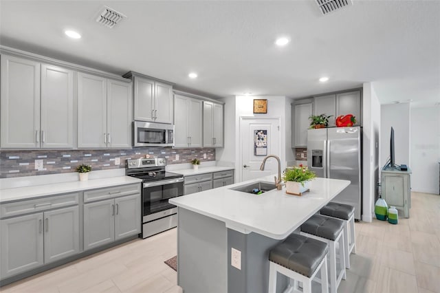 kitchen featuring a kitchen breakfast bar, stainless steel appliances, sink, gray cabinets, and an island with sink