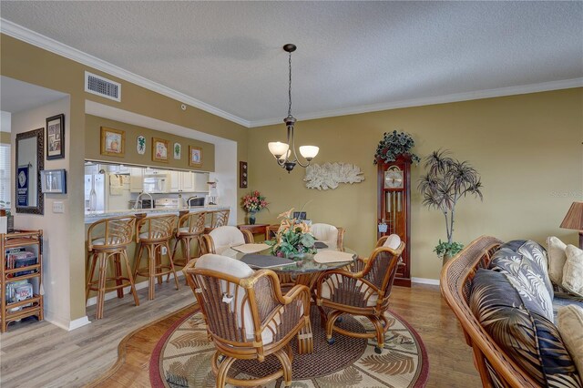 dining room with a chandelier, a textured ceiling, light hardwood / wood-style flooring, and ornamental molding