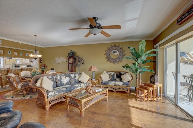 living room with a textured ceiling, light hardwood / wood-style flooring, ceiling fan with notable chandelier, and ornamental molding