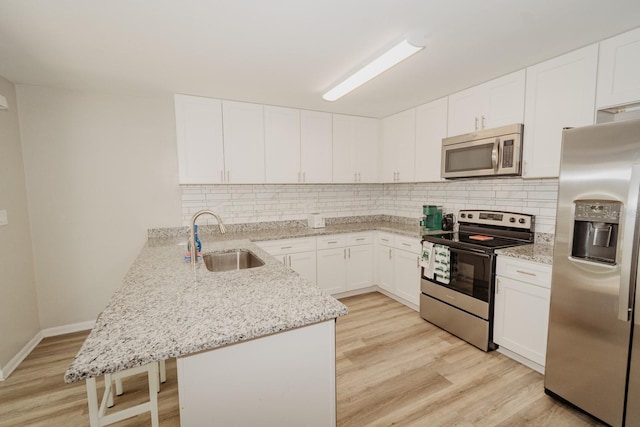 kitchen featuring white cabinets, sink, light stone countertops, kitchen peninsula, and stainless steel appliances