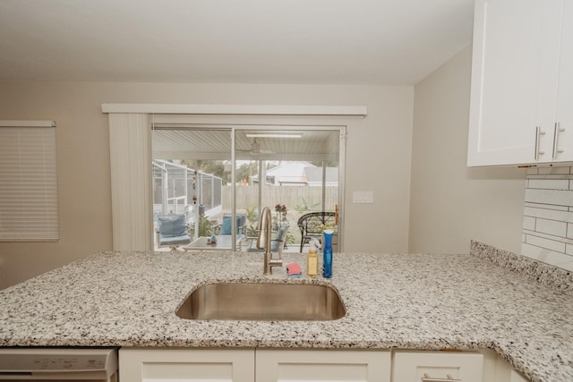 kitchen with dishwashing machine, white cabinetry, light stone counters, and sink