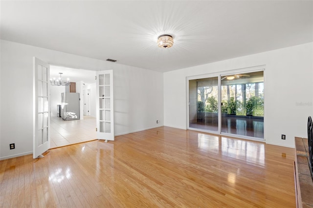 unfurnished room featuring french doors, an inviting chandelier, and light wood-type flooring