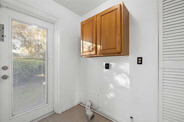 washroom with electric dryer hookup, light tile patterned floors, and cabinets