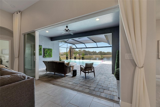 view of patio featuring ceiling fan, a lanai, and a water view