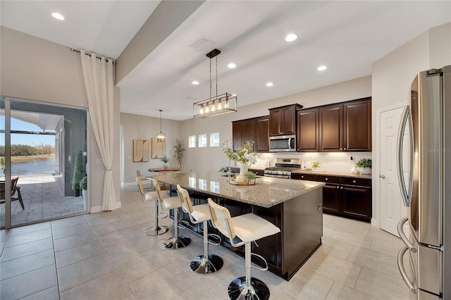 kitchen with appliances with stainless steel finishes, light stone counters, a breakfast bar, decorative light fixtures, and a kitchen island