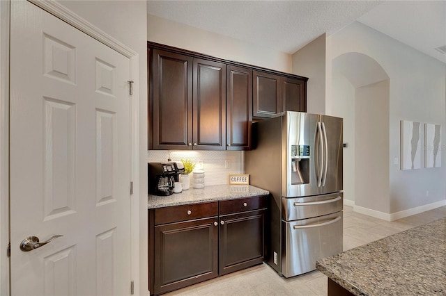 kitchen with decorative backsplash, stainless steel refrigerator with ice dispenser, light stone countertops, dark brown cabinetry, and light tile patterned flooring