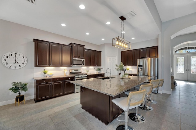 kitchen with sink, french doors, stainless steel appliances, light stone counters, and an island with sink