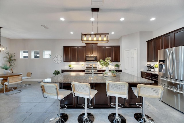 kitchen featuring light stone counters, pendant lighting, a breakfast bar, a center island with sink, and appliances with stainless steel finishes