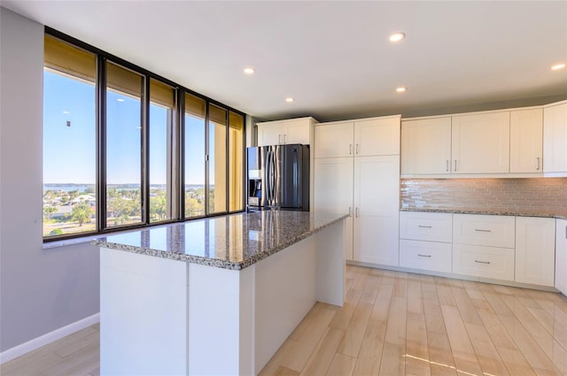 kitchen featuring tasteful backsplash, a kitchen island, stone counters, stainless steel fridge with ice dispenser, and white cabinetry