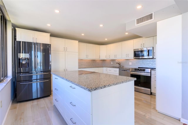 kitchen with white cabinetry, a center island, stainless steel appliances, and light hardwood / wood-style floors