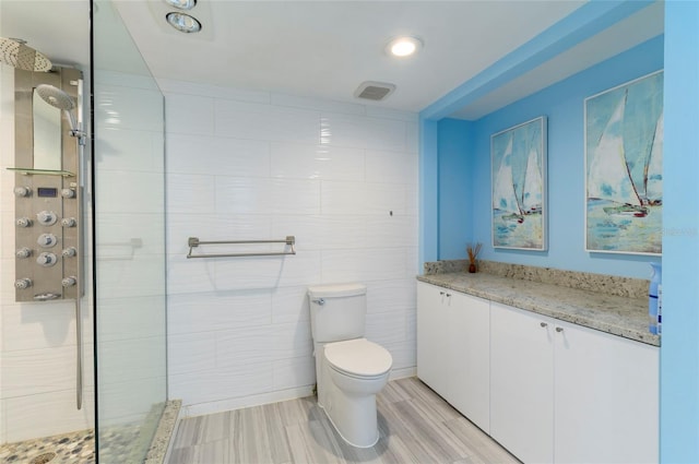 bathroom with a tile shower, vanity, hardwood / wood-style flooring, tile walls, and toilet