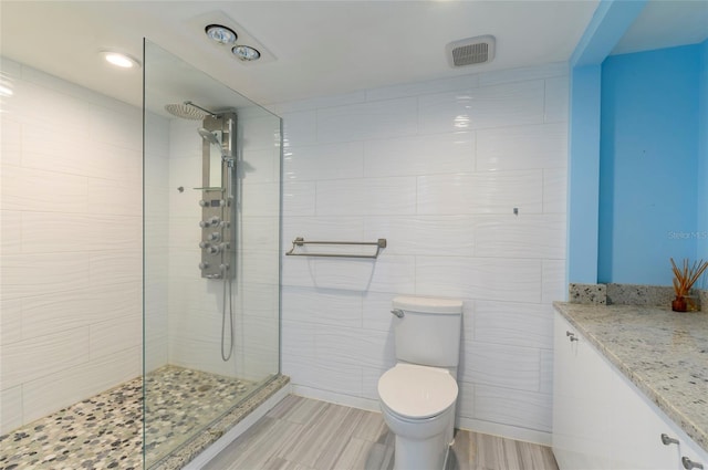 bathroom featuring toilet, tiled shower, and tile walls