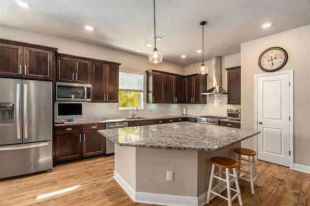 kitchen with stone counters, sink, wall chimney exhaust hood, a kitchen island, and stainless steel appliances