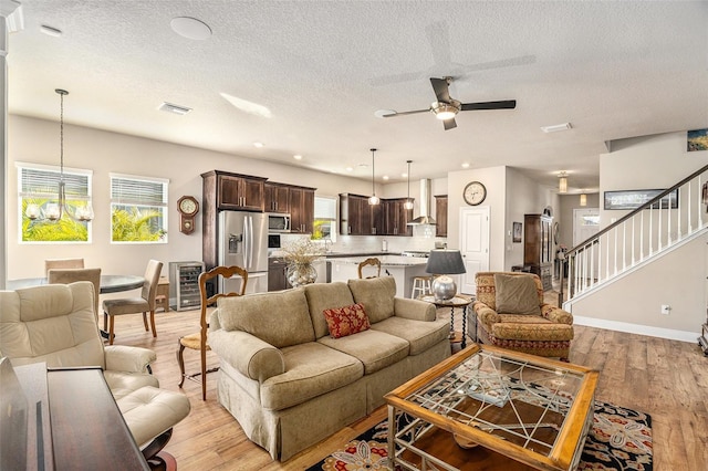 living room with a textured ceiling, light hardwood / wood-style floors, and ceiling fan with notable chandelier