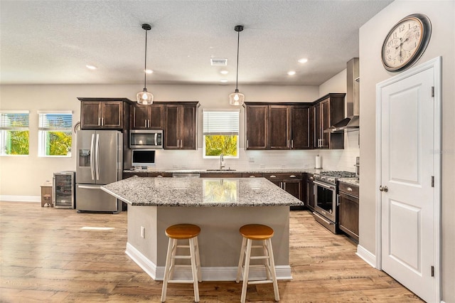 kitchen featuring sink, a kitchen island, wall chimney range hood, and appliances with stainless steel finishes