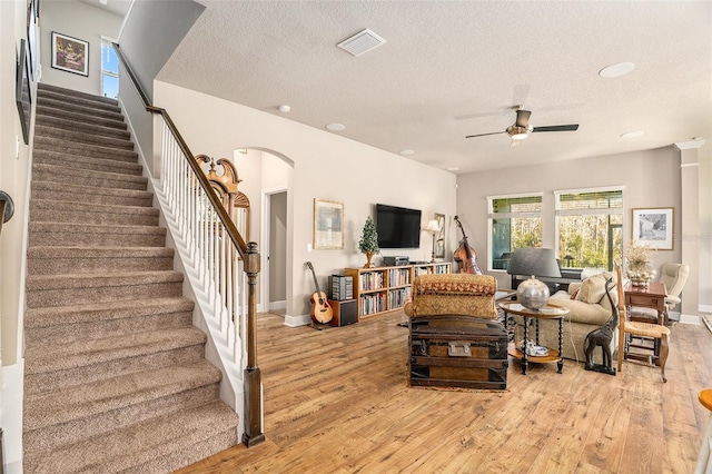 living room with a textured ceiling, light wood-type flooring, and ceiling fan