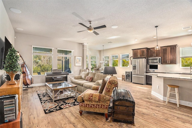 living room with wine cooler, plenty of natural light, light hardwood / wood-style floors, and a textured ceiling