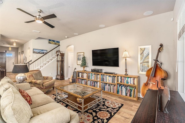 living room with ceiling fan, light wood-type flooring, and a textured ceiling