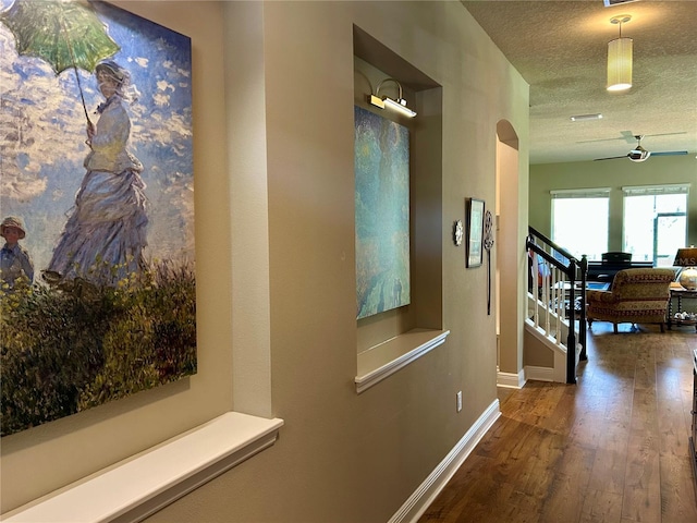 hall with baseboards, arched walkways, hardwood / wood-style flooring, stairs, and a textured ceiling